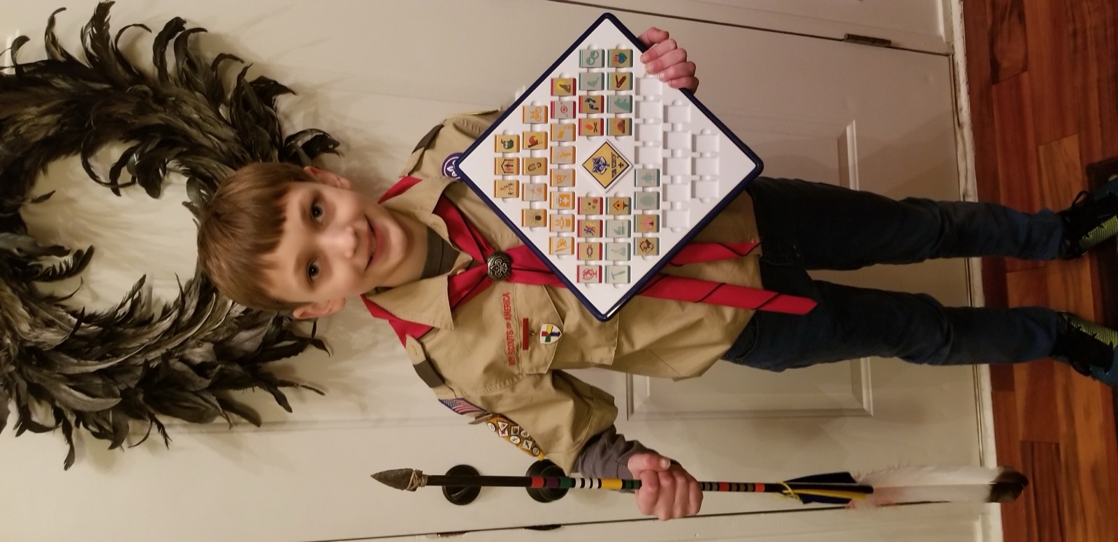 Quinn holding a Cub Scout adventure board covered in earned belt loops and pins.